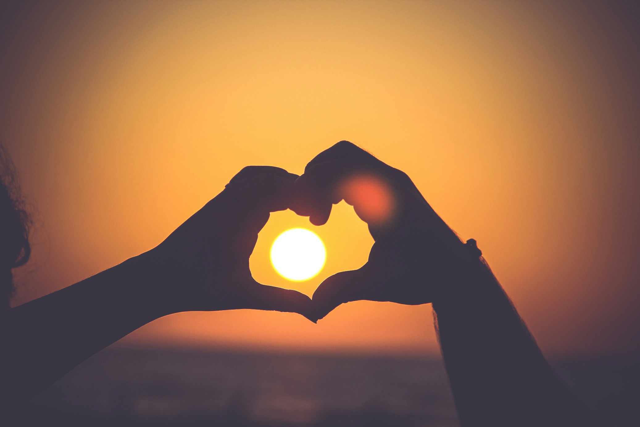 hands making heart with sunset in background